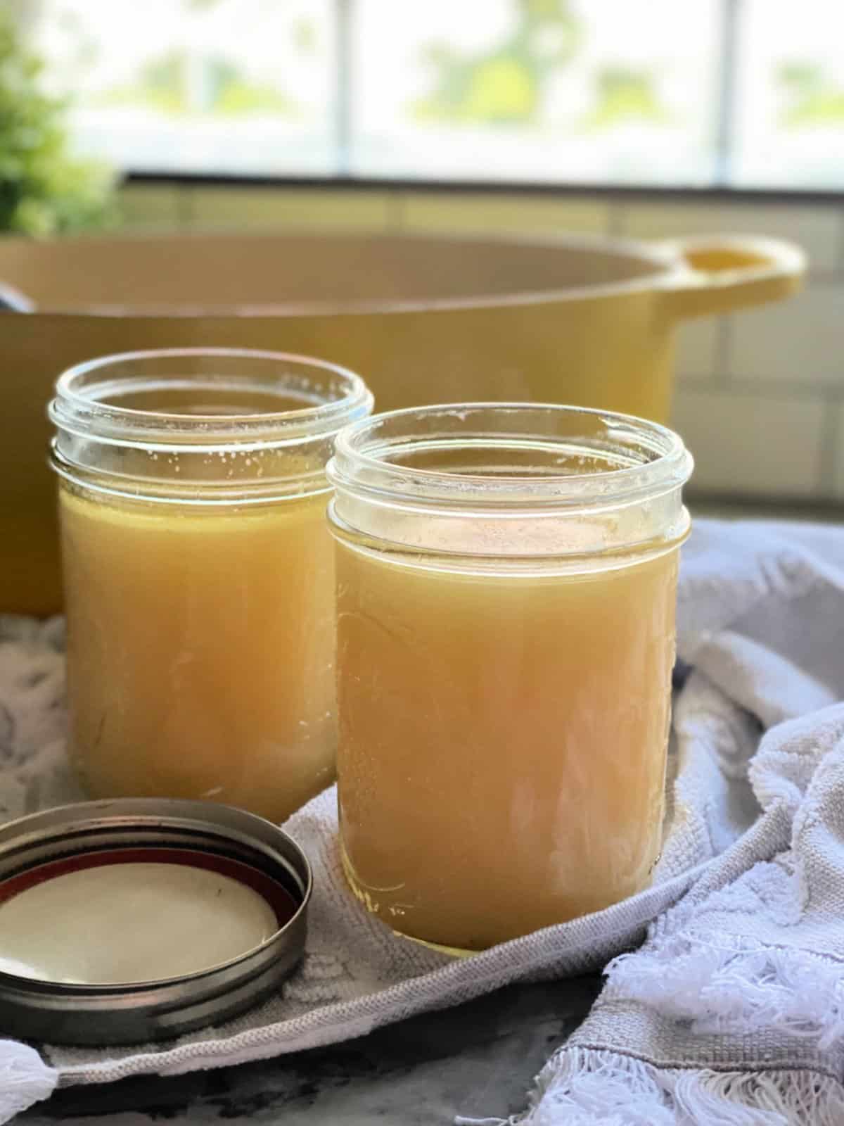 Two mason jars filled with yellow liquid with a yellow pot in te background.