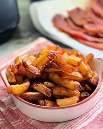 White dish with fried breakfast potatoes inside sitting on red and white towel