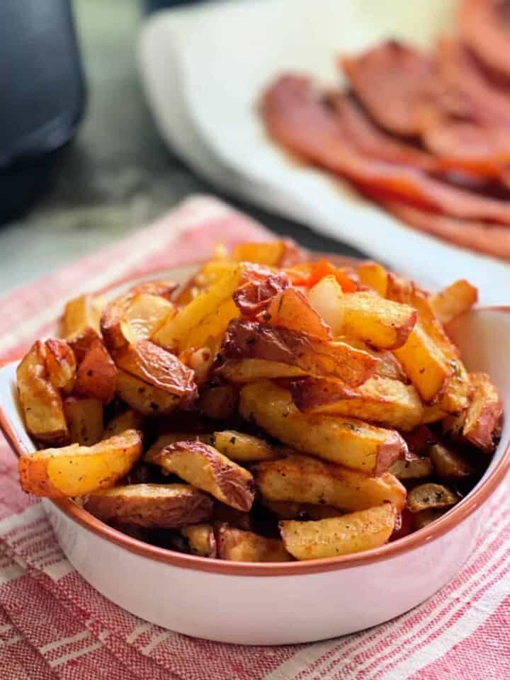 White dish with fried breakfast potatoes inside sitting on red and white towel