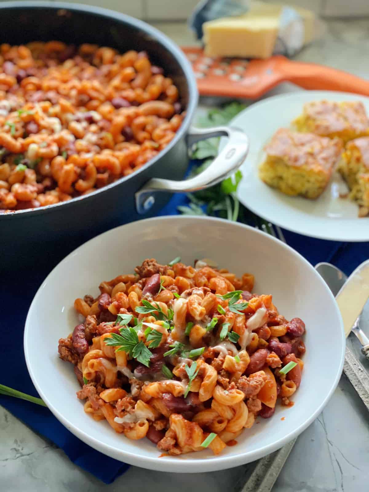 Chili pasta in white bowl with skillet slices of cornbread in background