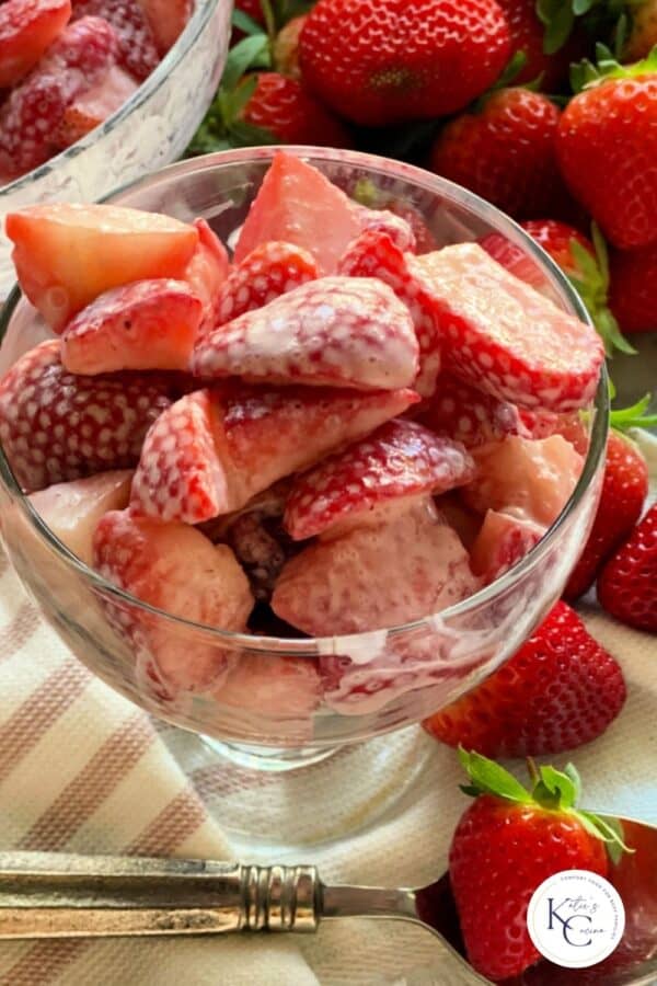 Strawberries and cream in glass cup with fresh strawberries in background