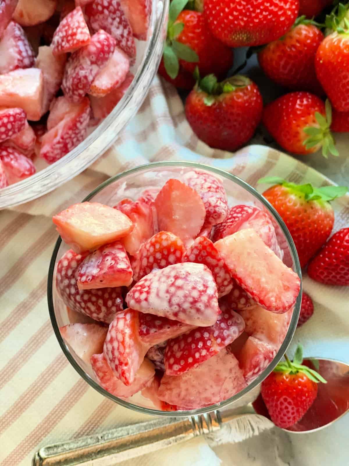 Strawberries and cream in serving dish and bowl with fresh strawberries in background