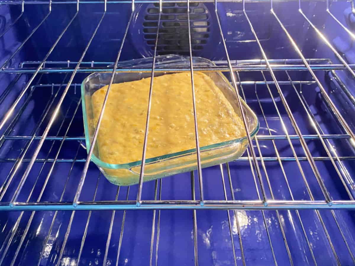 cornbread batter in square glass baking dish sitting in middle rack of oven