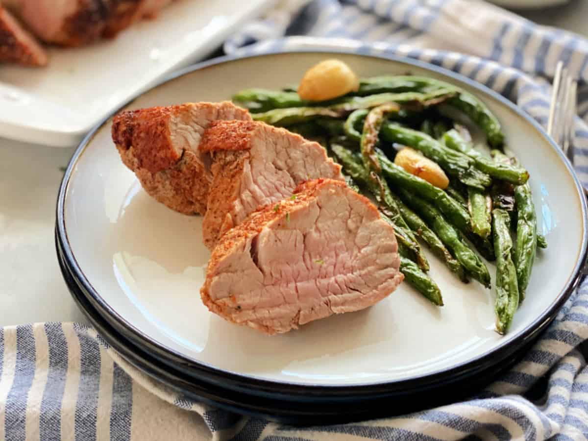 three slices of pork tenderloin with asparagus on white plate