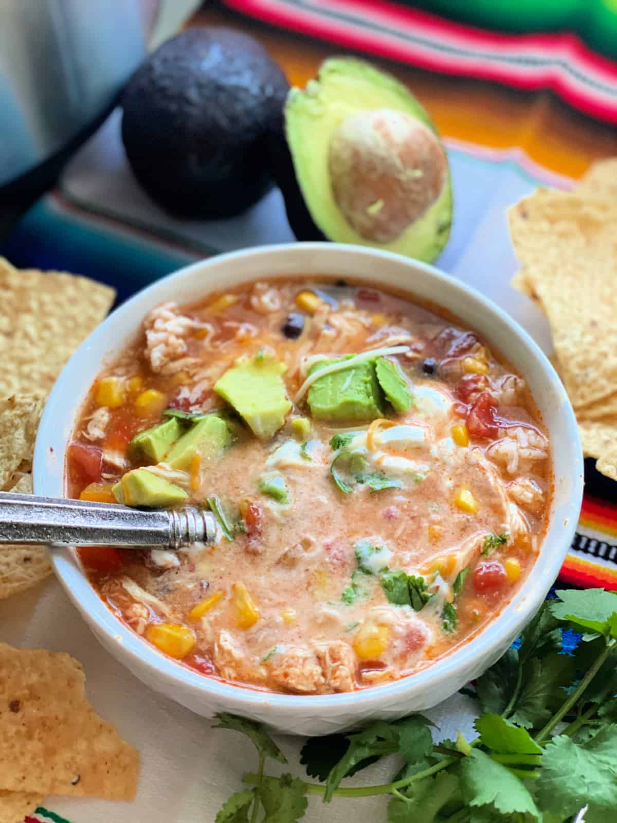 Chicken enchilada soup in white bowl on top of colorful blanket