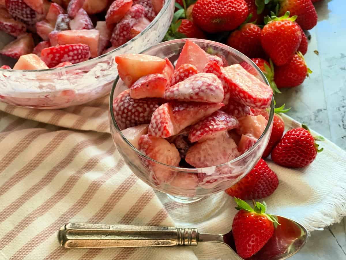 Strawberries and cream in serving dish and bowl with fresh strawberries in background