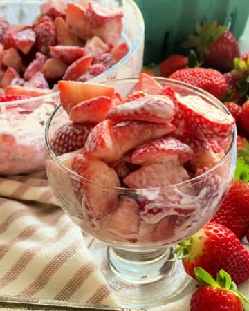 Strawberries and cream in serving dish and bowl on top of white and pink kitchen towel