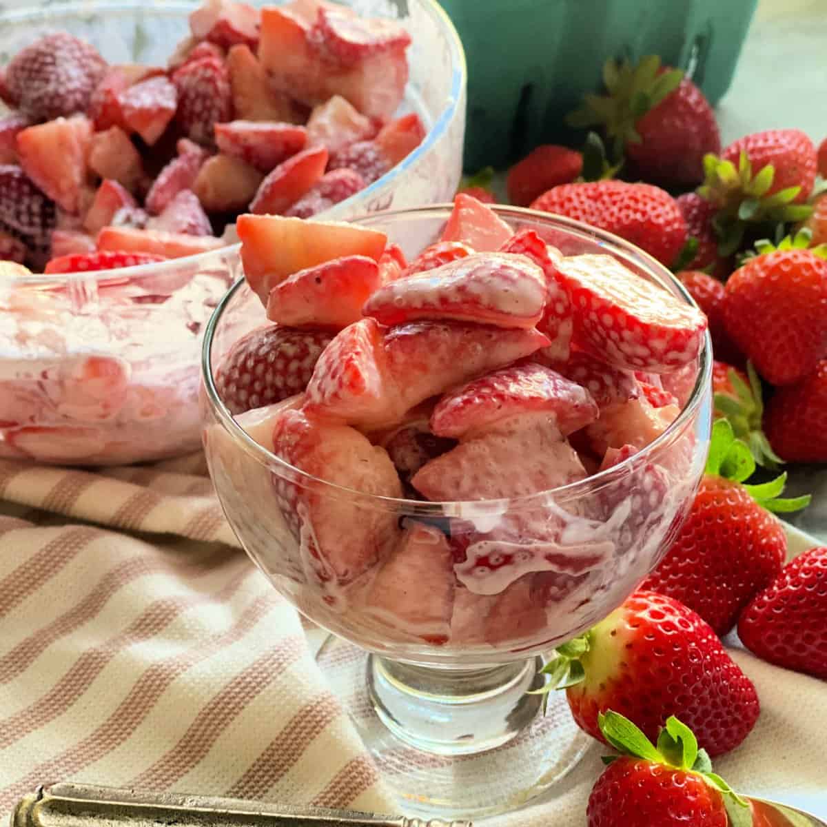 Strawberries and cream in serving dish and bowl on top of white and pink kitchen towel