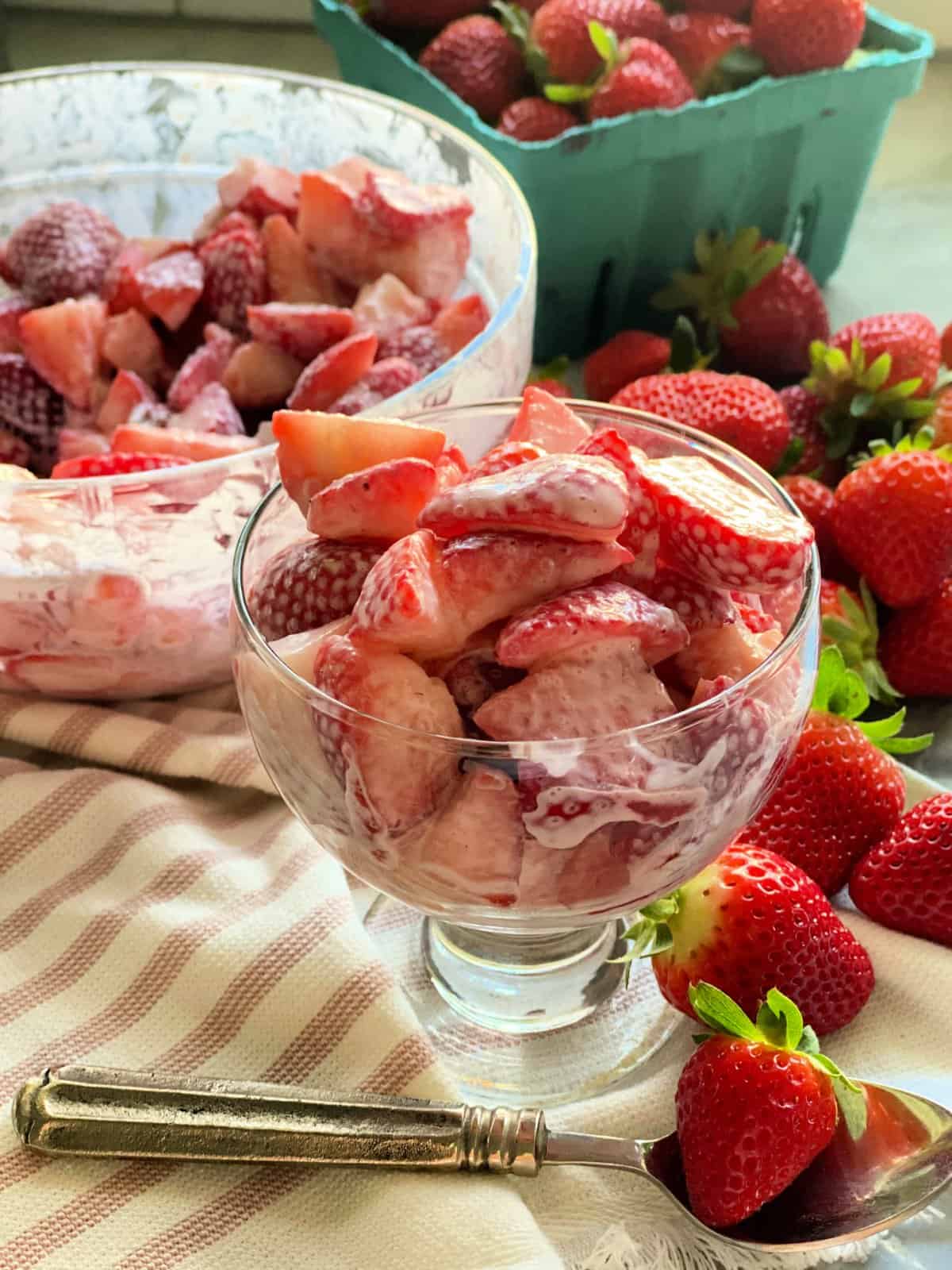 Strawberries and cream in serving dish and bowl on top of white and pink kitchen towel