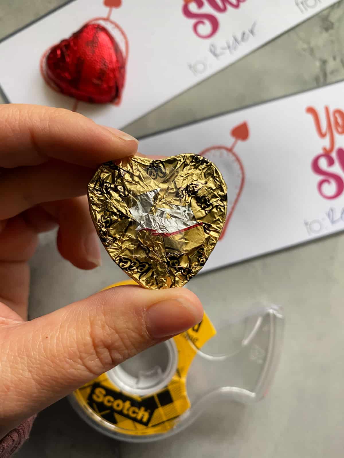 Hand holding a heart candy with tape on the back.