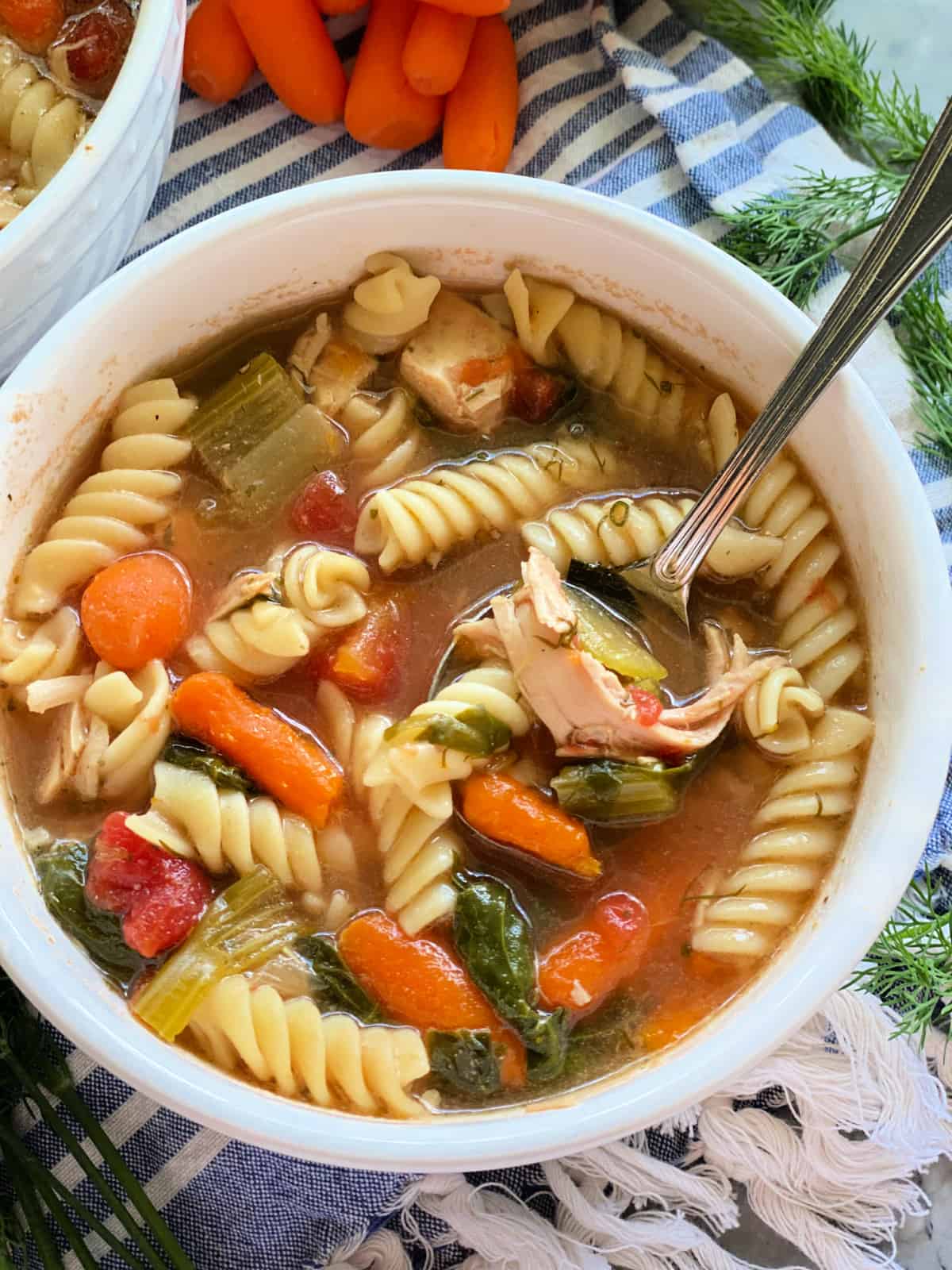 Rotisserie chicken noodle soup in white bowl with spoon