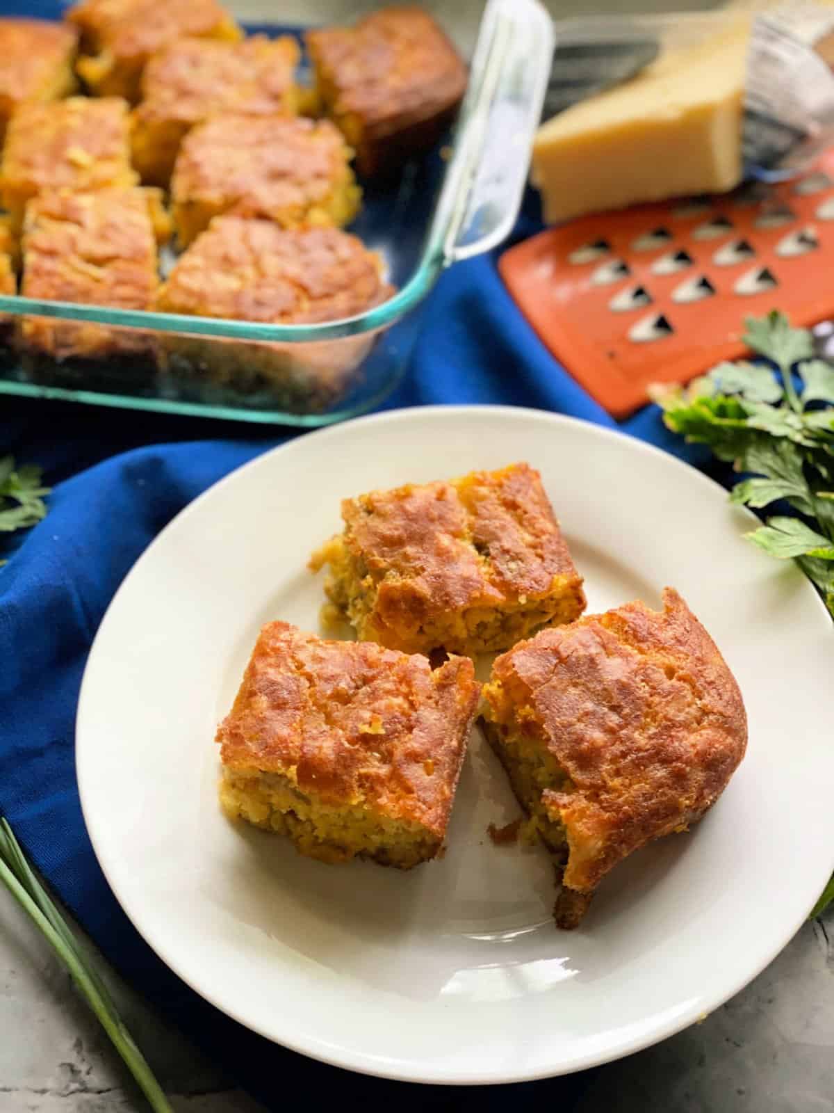 three cornbread slices on white plate with baking dish filled with more cornbread in the background