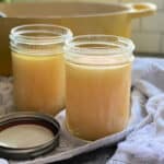 Two glass jars of chicken stock with yellow dutch oven in background