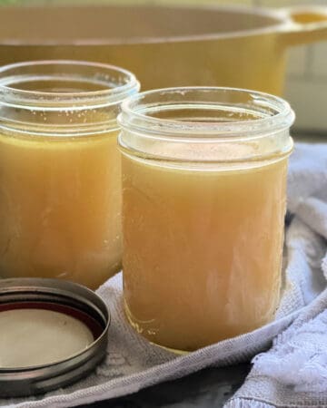 Two glass jars of chicken stock with yellow dutch oven in background