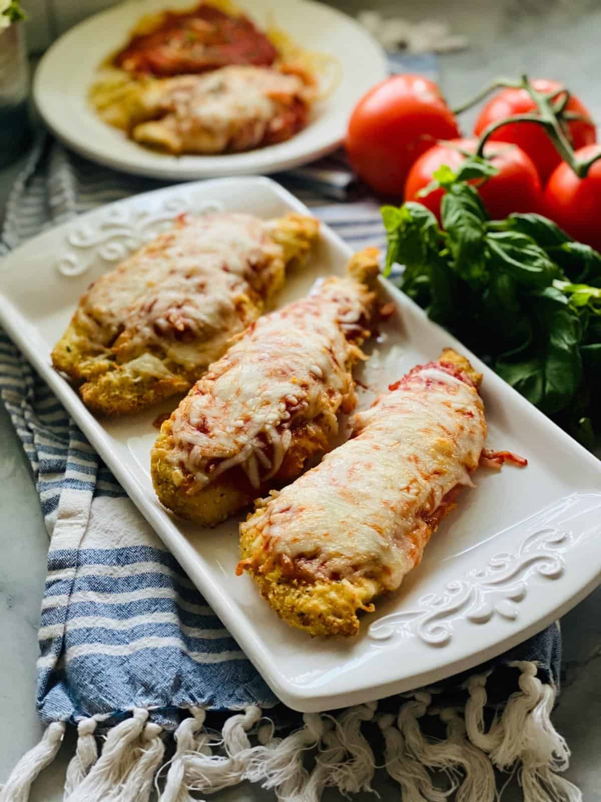Three pieces of chicken parmesan on a white serving dish