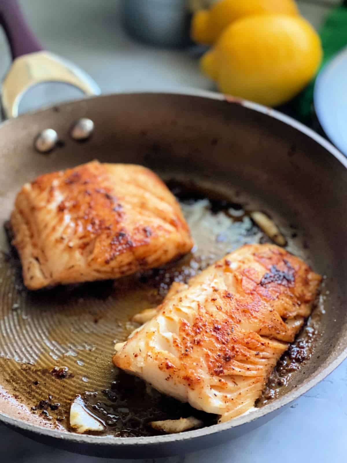 Two black cod fish fillets cooking on a skillet
