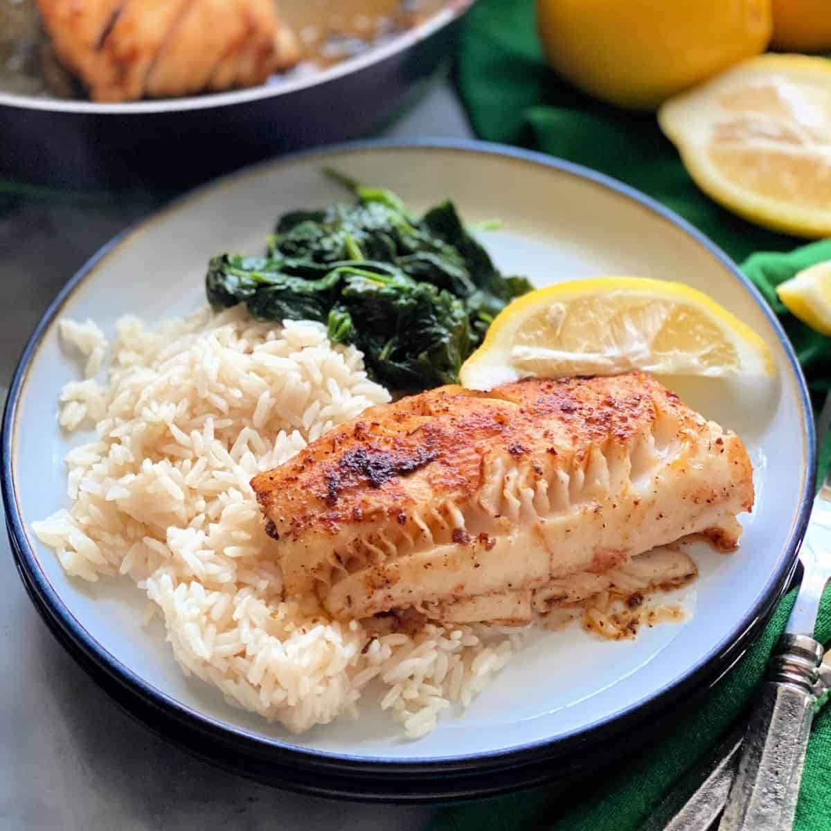 White plate with a piece of cod, white rice, spinach, and a lemon.