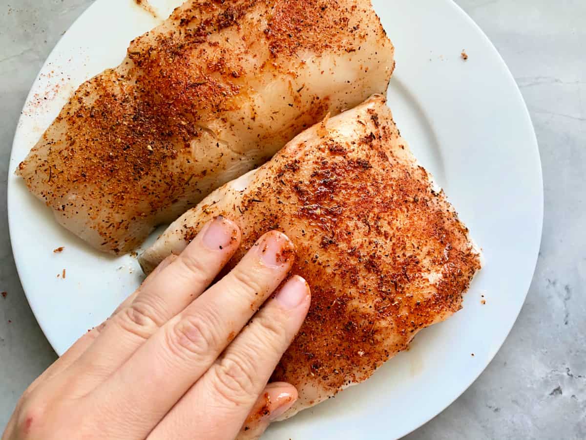 Seasoning rubbed on two black cod fish fillets on a white plate