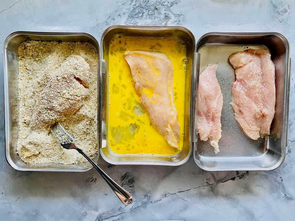 Breading process for chicken parmesan: seasoned chicken on the left, egg mixture in the middle, breading on the left.