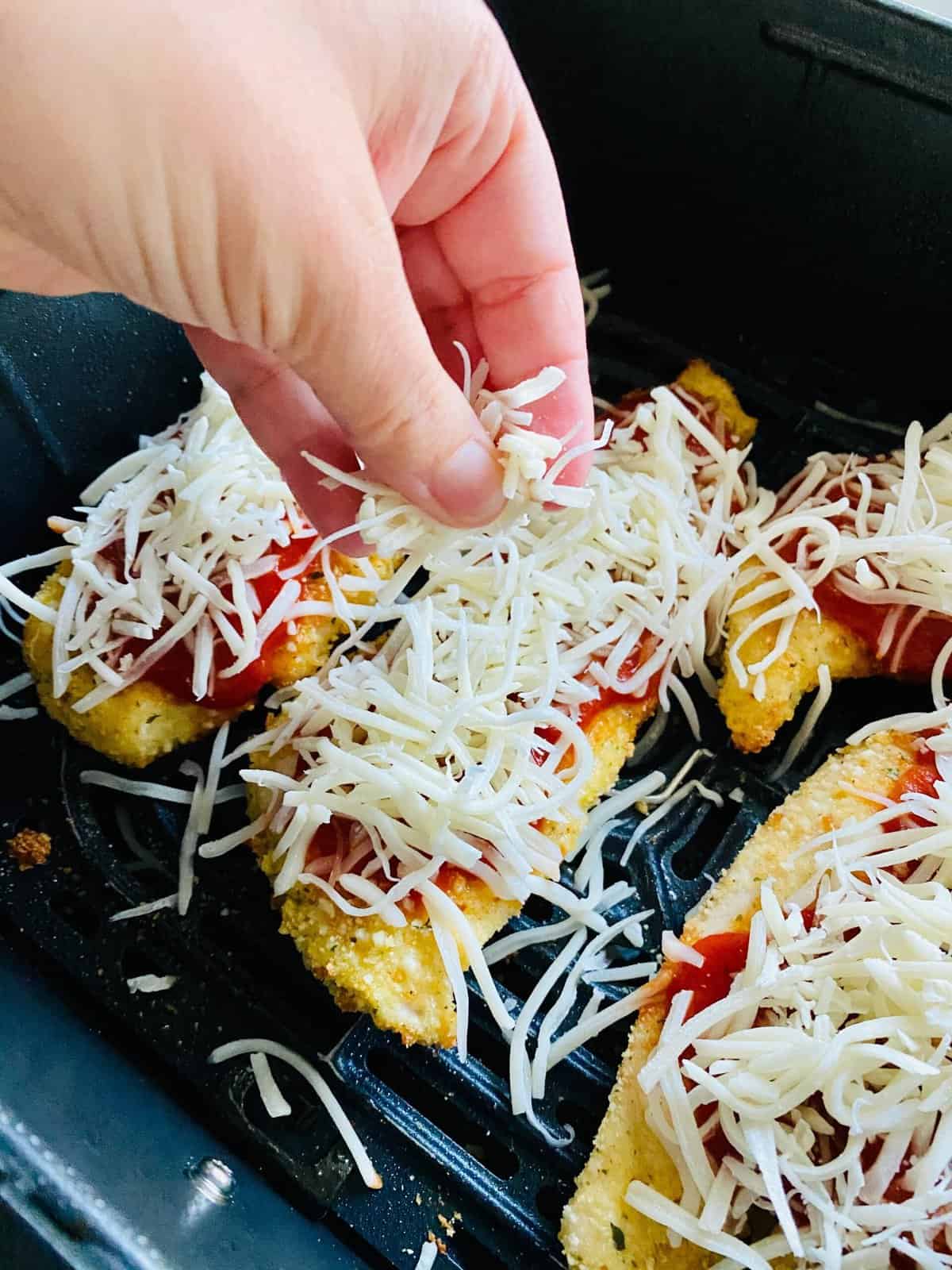 Breaded chicken breast topped with tomato sauce and cheese in air fryer basket