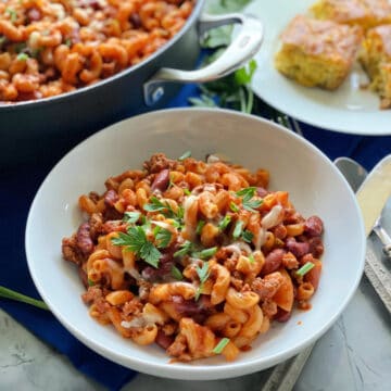 White bowl with pasta and ground beef with red sauce with green onions and parsley on top.