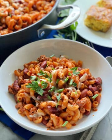 White bowl with pasta and ground beef with red sauce with green onions and parsley on top.