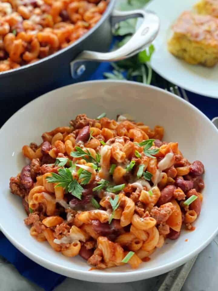 White bowl with pasta and ground beef with red sauce with green onions and parsley on top.