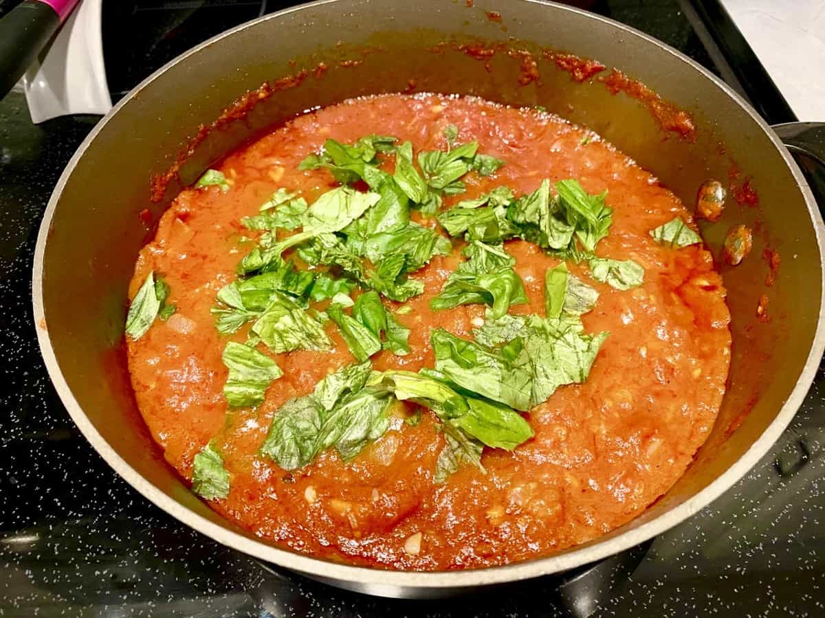 Pasta sauce topped with basil cooking in a stainless steel pot