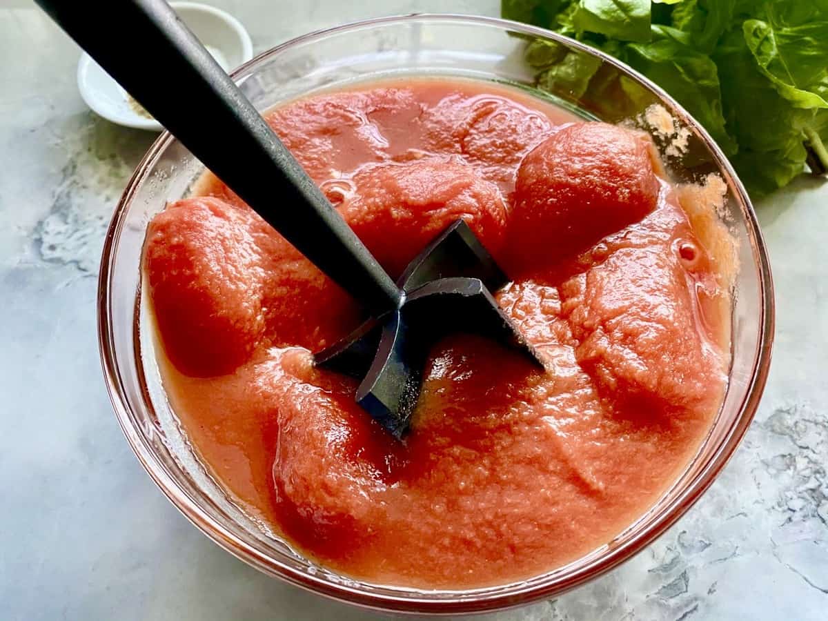 Whole peeled tomatoes from can getting crushed in glass mixing bowl