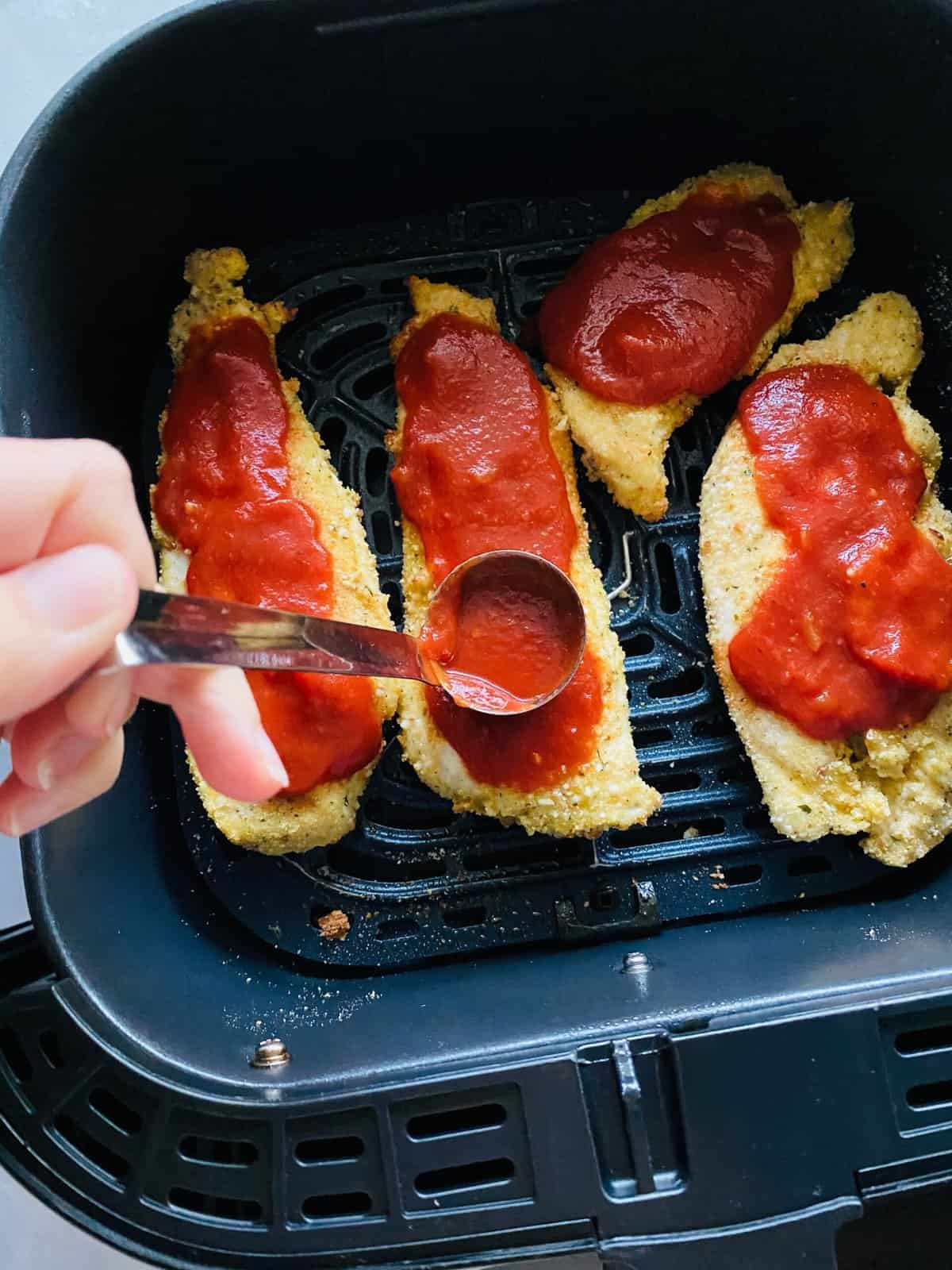 Tomato sauce ladled over breaded chicken in air fryer basket