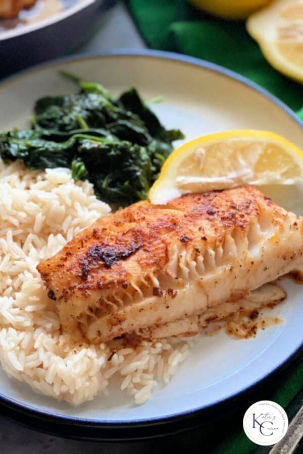 Blackened cod, white rice, spinach, and a lemon slice on a white plate