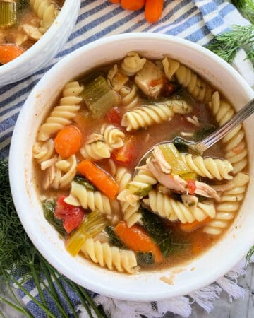 Top view of a white bowl filled with rotini pasta, vegetables, chicken and broth.