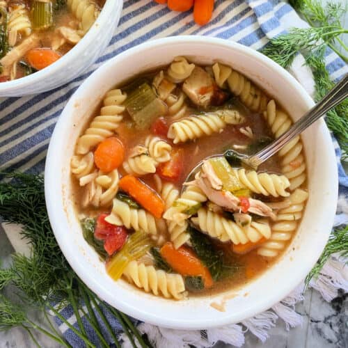 Top view of a white bowl filled with rotini pasta, vegetables, chicken and broth.