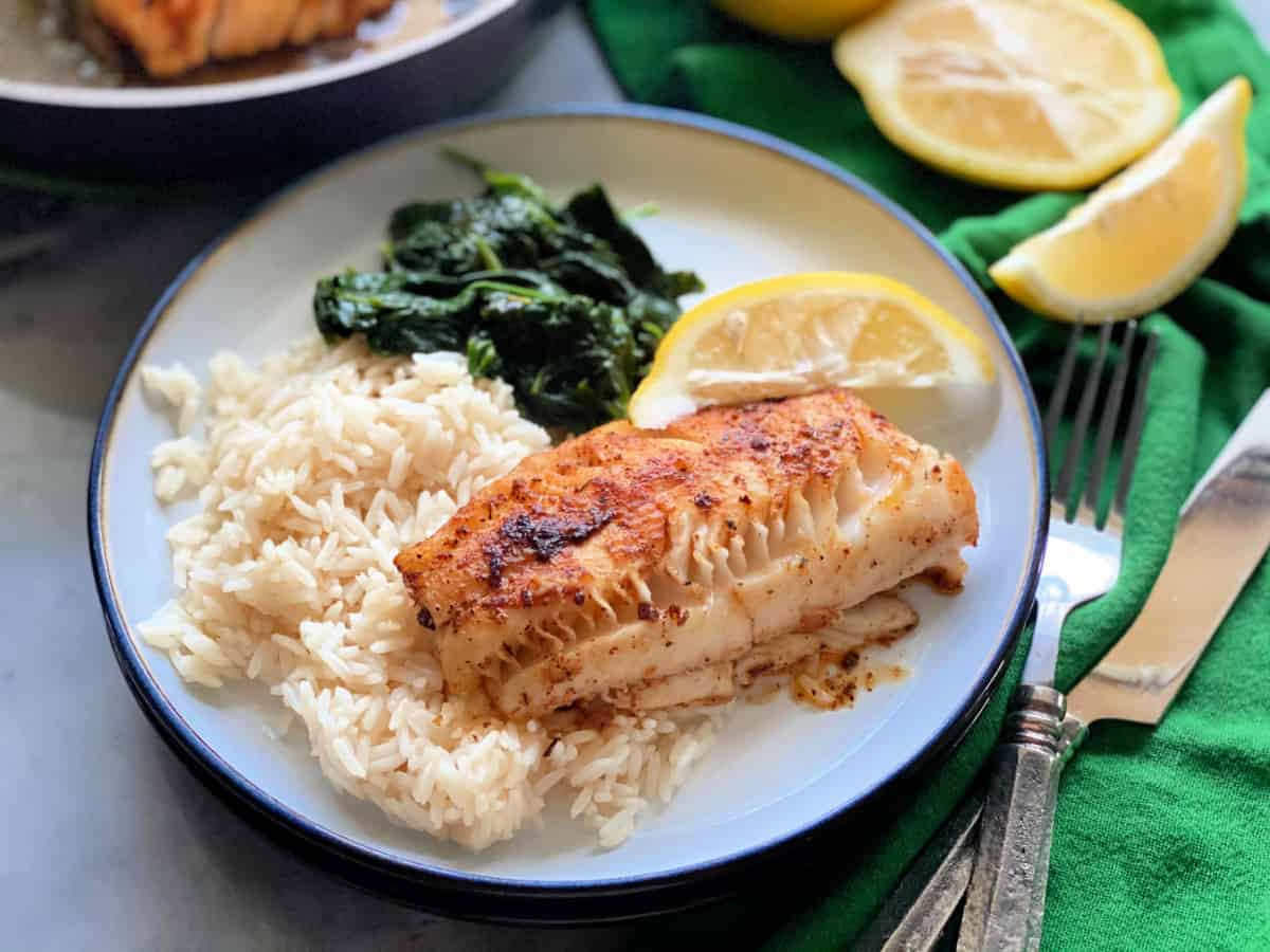 Blackened cod, white rice, spinach, and a lemon slice on a white plate