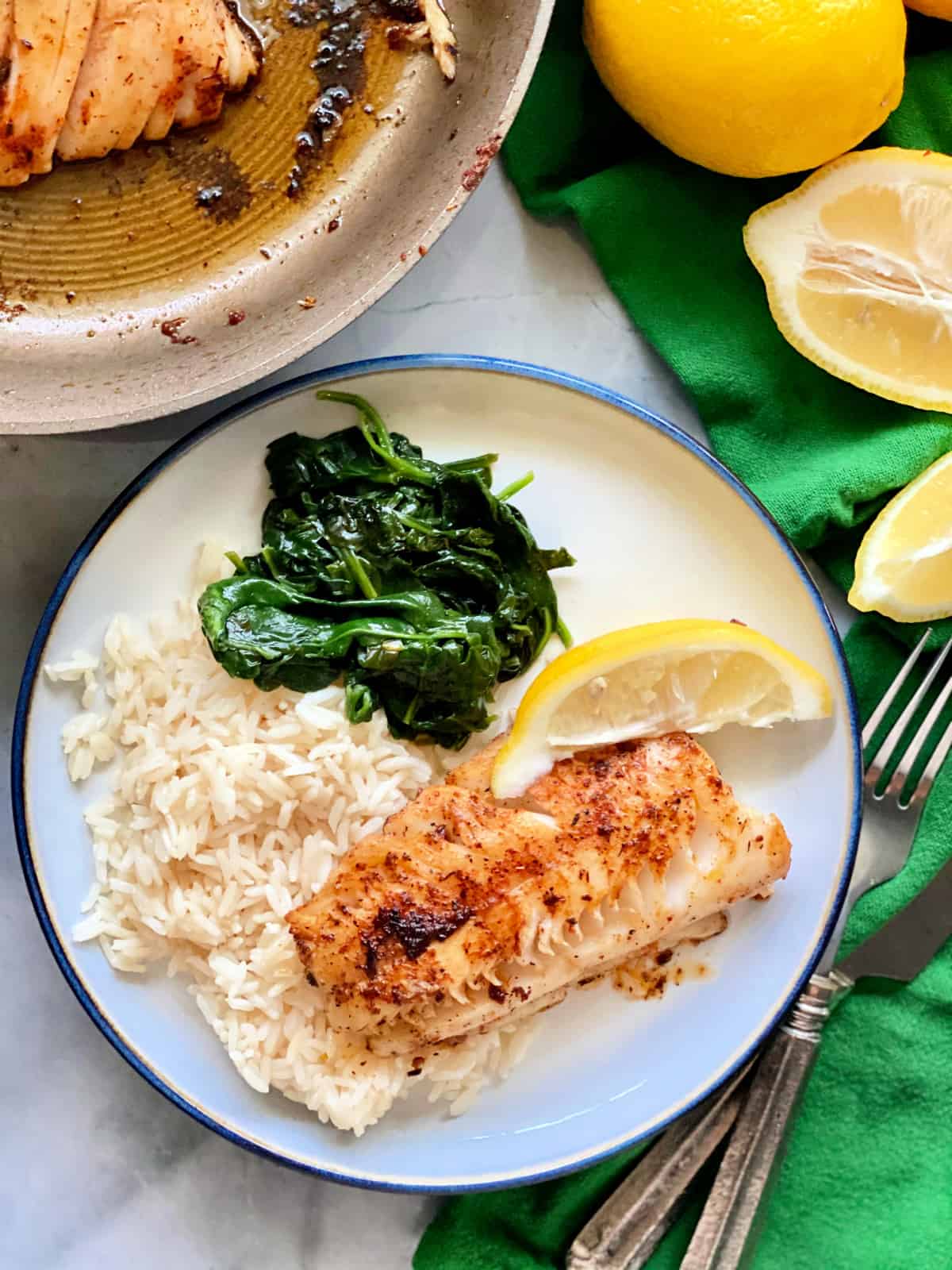 Top view shot of Blackened cod, white rice, spinach, and a lemon slice on a white plate