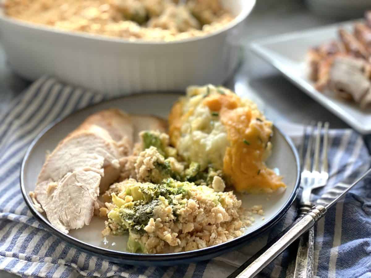 Broccoli casserole served on a white plate with turkey and mashed potatoes, casserole dish in the background
