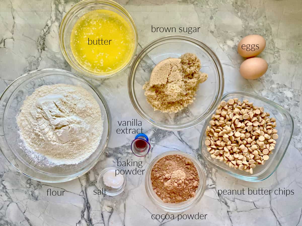 Ingredients on counter: flour, butter, brown sugar, eggs, vanilla extract, baking powder, cocoa powder, and peanut butter chips.