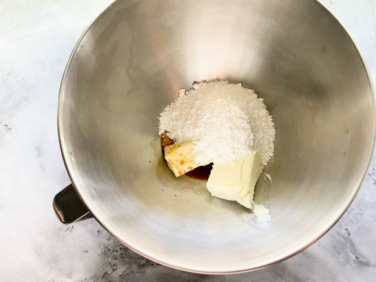 Metal mixing bowl with butter, vanill, and confectioners' sugar.