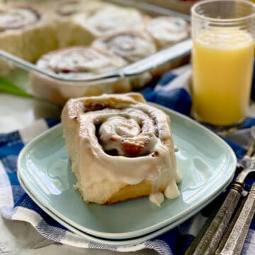 Two blue plates stacked with a thick cinnamon roll on top with orange juice in background.