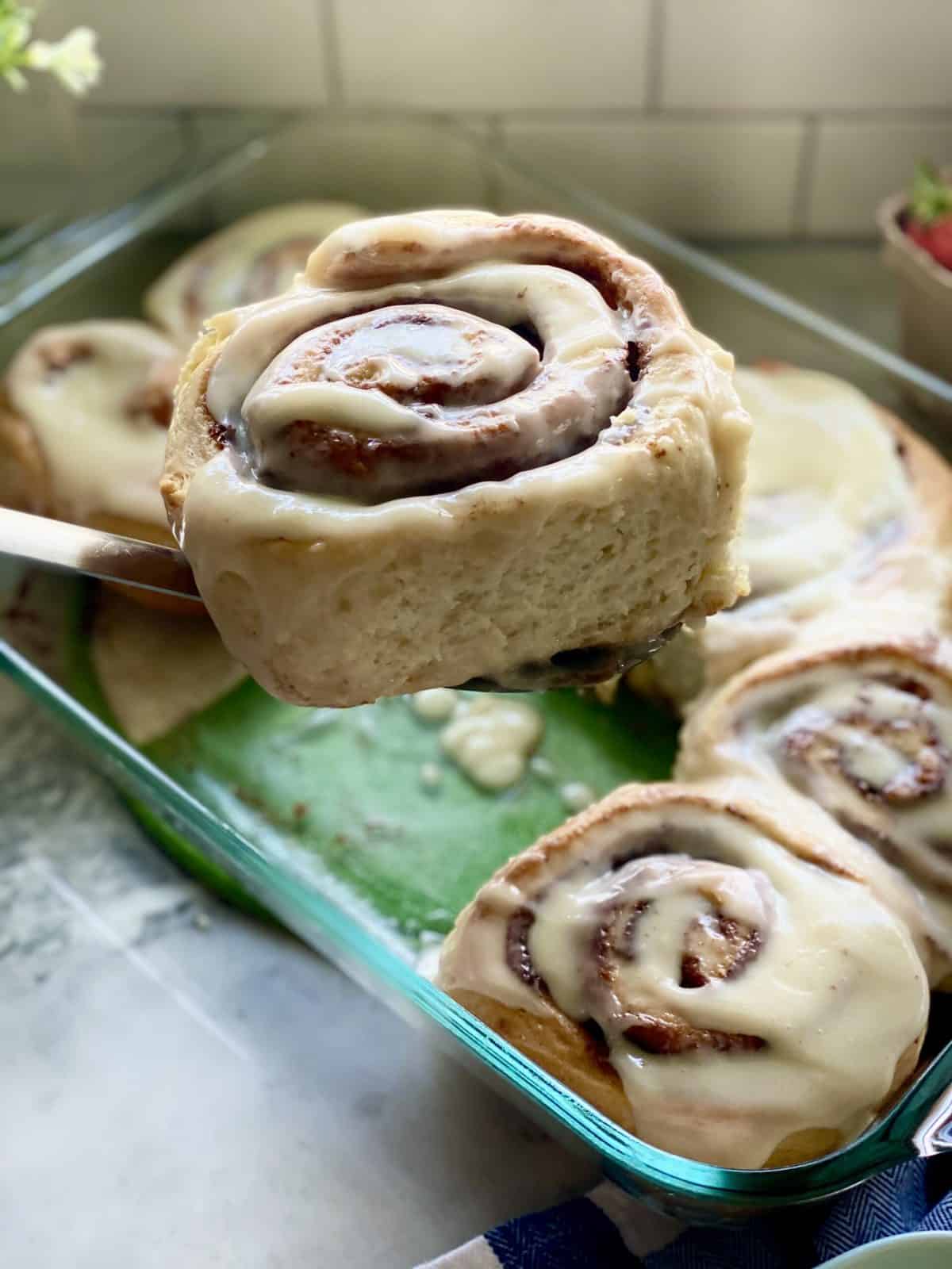 Spatula holding a cinnamon roll over a glass tray.