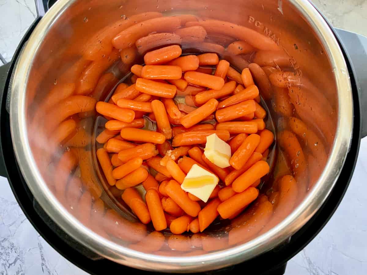 Top view of instant pot filled with babay carrots, butter and honey.