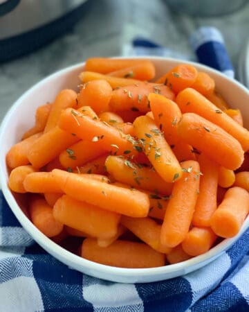 Square photo of a white bowl filled with cooked baby carrots.