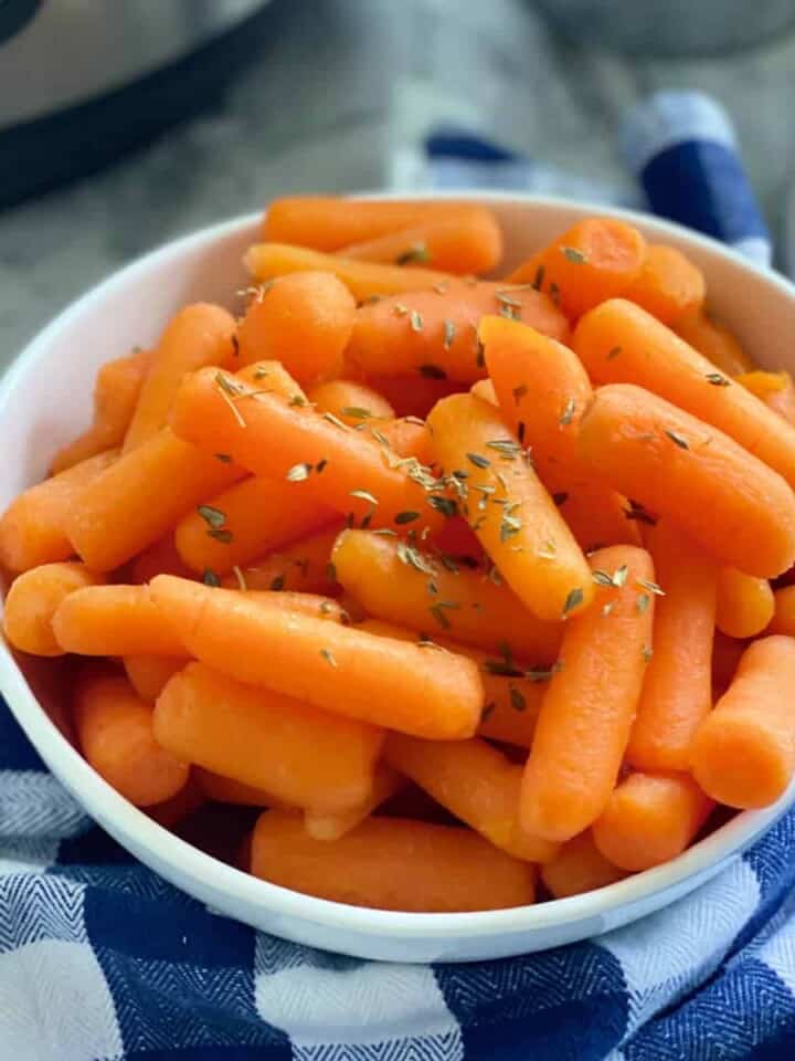 Square photo of a white bowl filled with cooked baby carrots.
