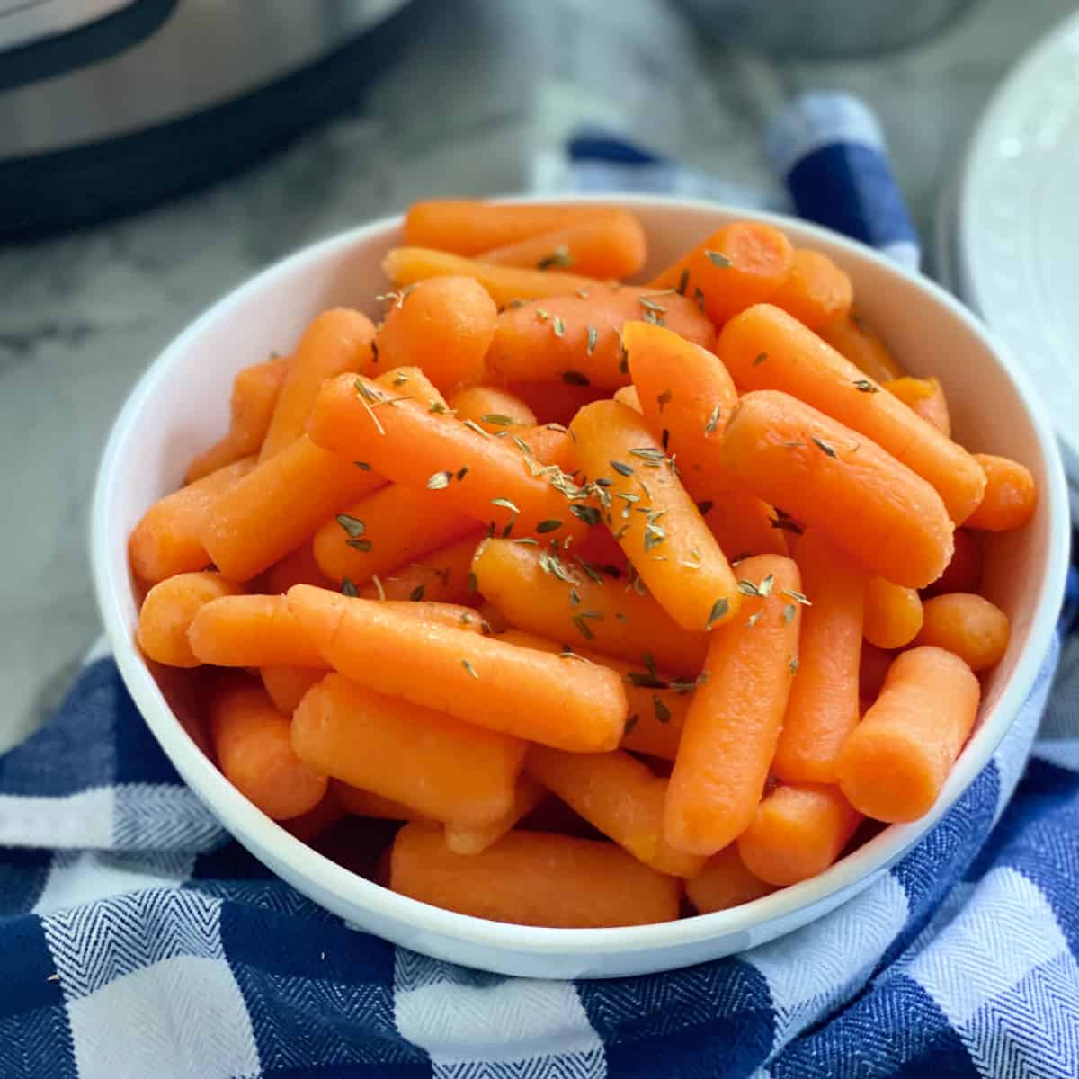 Square photo of a white bowl filled with cooked baby carrots.