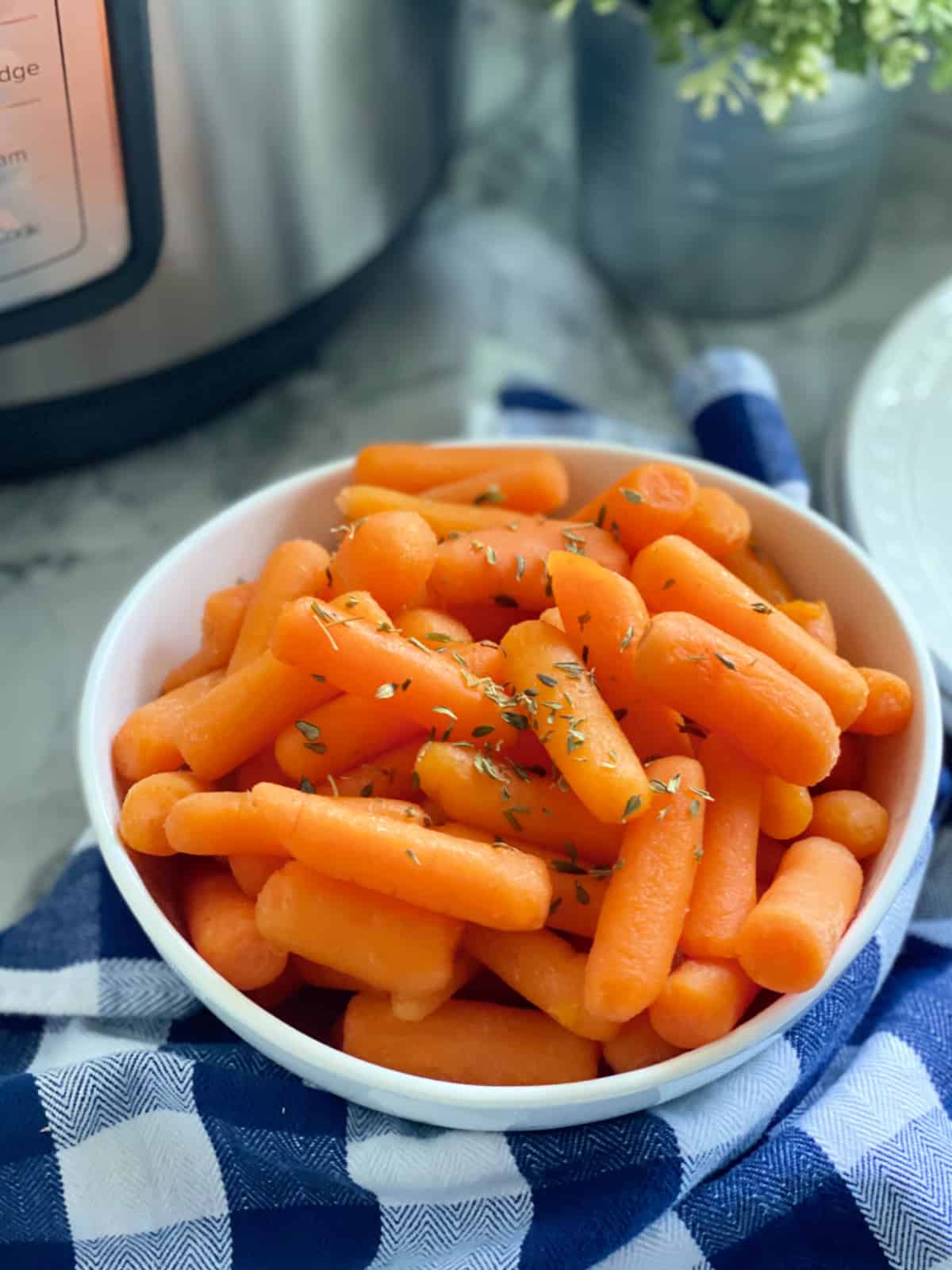White bowl filled with baby carrots with a blue and white checkered cloth next to it.