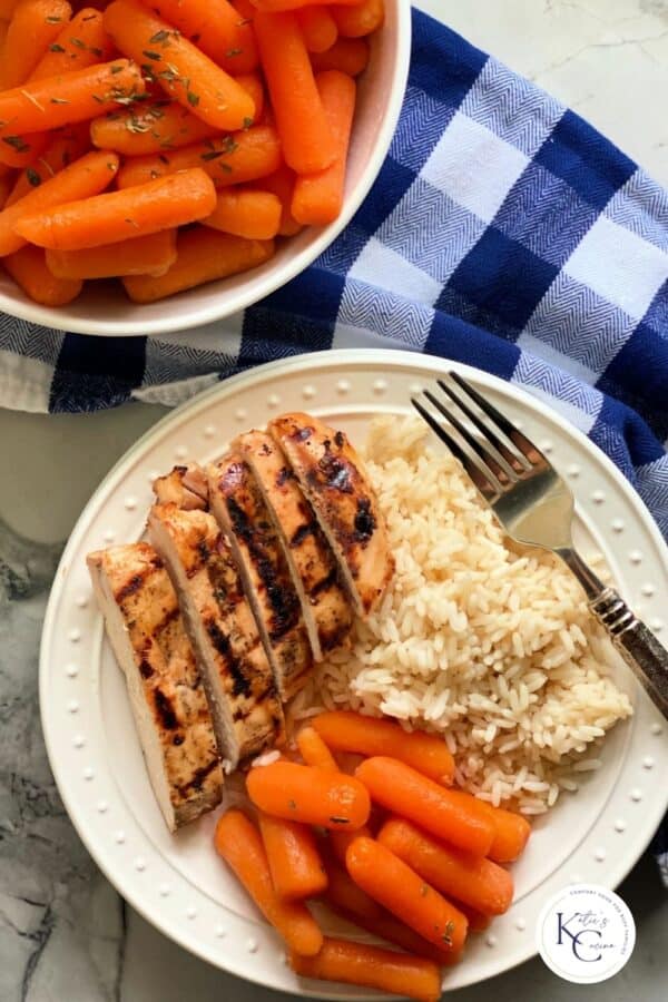 Top view of a white plate with carrots, grilled chicken and rice with logo on corner.