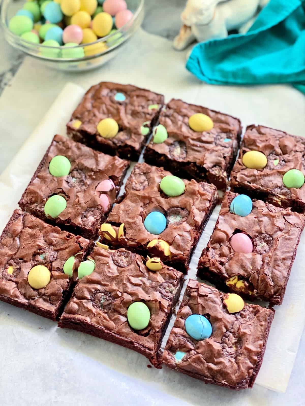 9 cut brownies with pastel egg candies in them on a marble countertop.