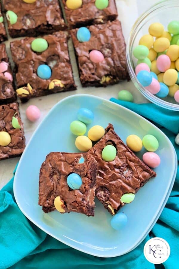Top view of a light blue square plate with 2 brownies cut with hardshell candies.