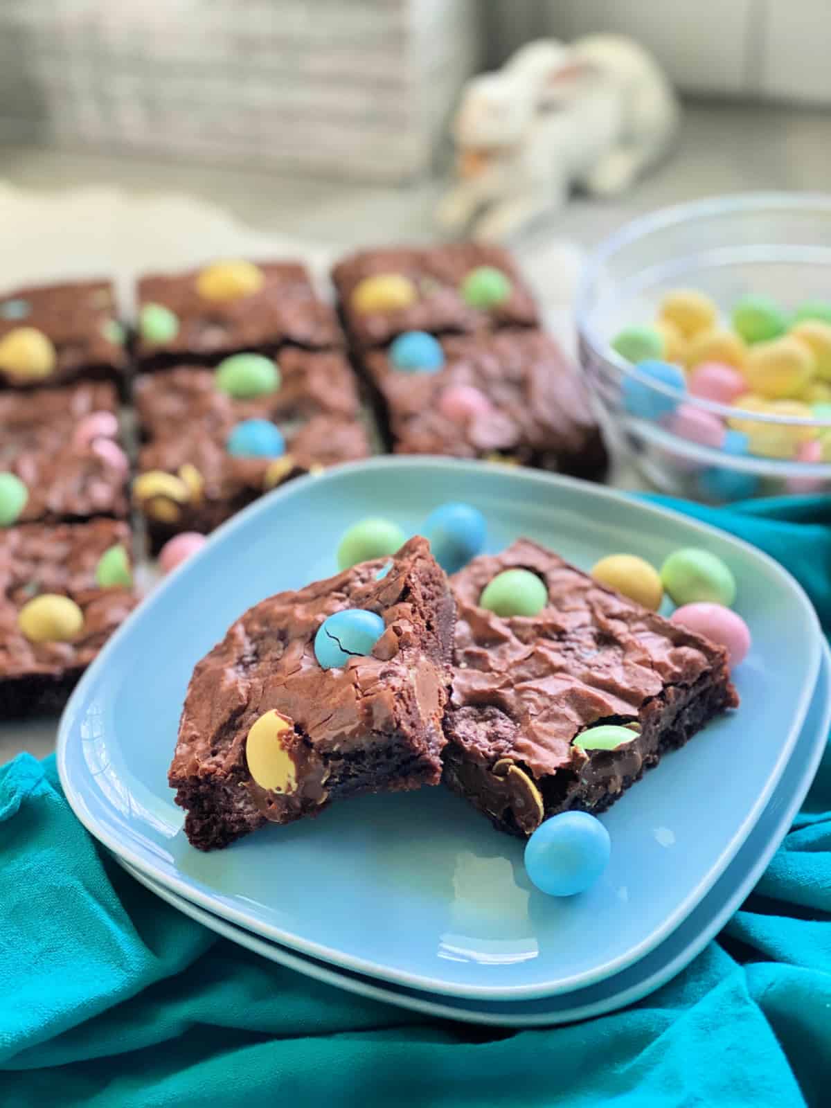 Two blue plates stacked with two brownies and egg candies on it.