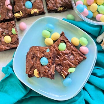 Square photo of a blue plate with two brownies and colored eggs pressed in.